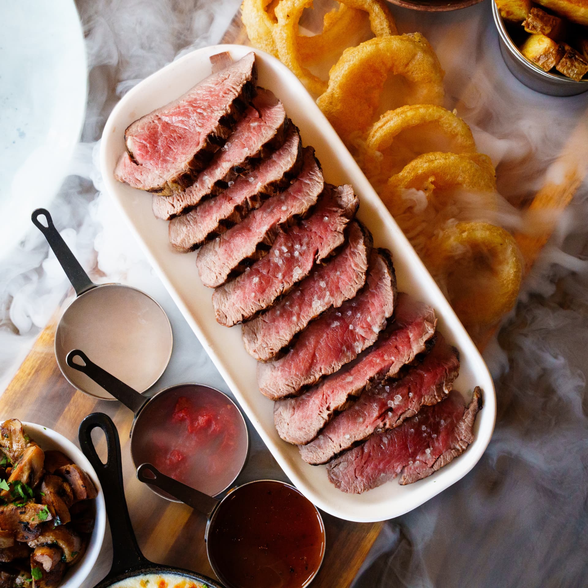 Sliced steak sharing platter with sauces and onion rings